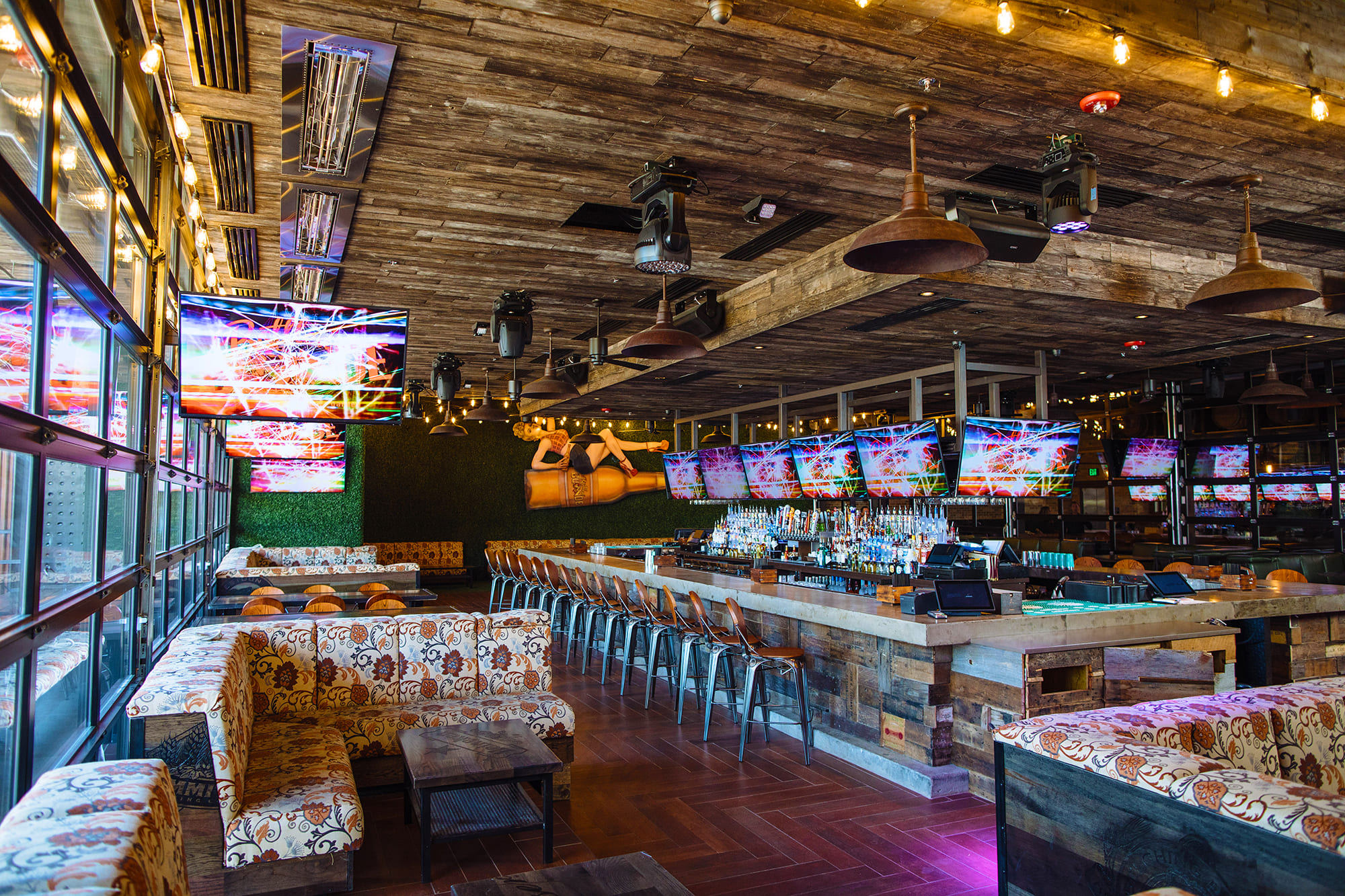 Modern bar interior with wood finishes, metal stools, and flat-screen TVs.