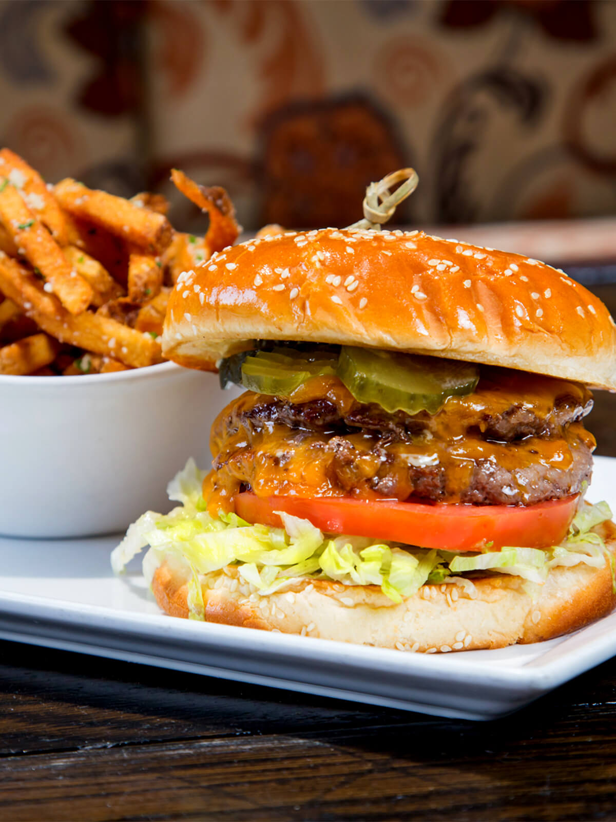 Close-up of a double cheeseburger with melted cheese, lettuce, tomato, and pickles, served with fries.